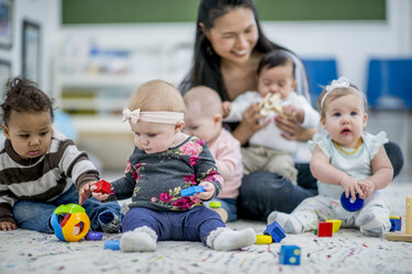 a childcare worker with a group of five babies and toddlers