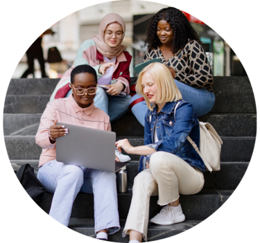 Students sit on the steps near the college and look at the laptop and digital tablet and talk