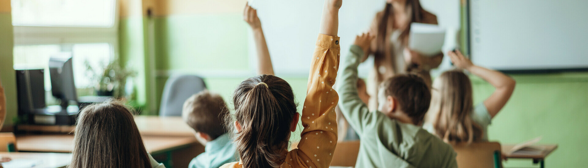 young students in classroom hands up with teacher