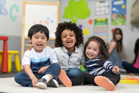 three early learning students smiling in a classroom