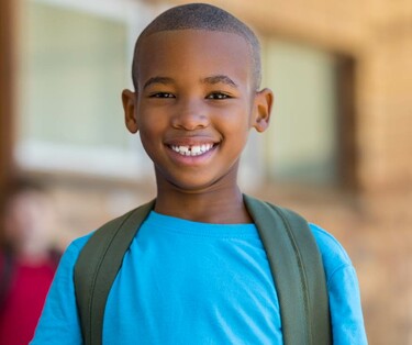 a young boy wearing a backpack, smiling outside