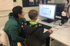 a teacher assisting a grade one student with a computer art project