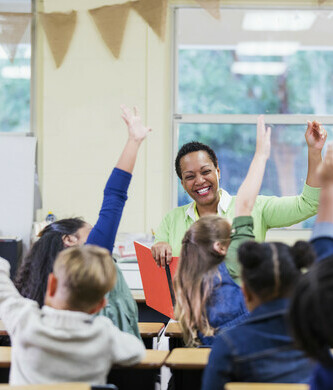 teacher in classroom with students raising their hands