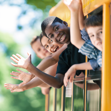 smiling kids waving out from yellow school bus